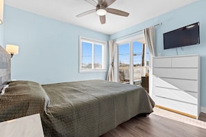 Quarto com cama, ventoinha no teto, televisão e janela com cortinas.