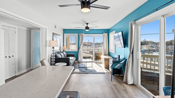 Un salon moderne doté d’un ventilateur de plafond, d’un canapé, d’une table basse et offrant une vue sur la ville grâce à de grandes fenêtres.