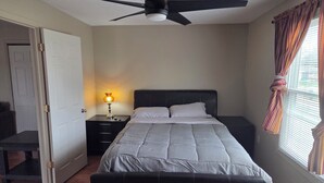 A bedroom with a bed, a nightstand, a lamp, a ceiling fan, and a window with curtains. - Cozy 1-bedroom apartment in pleasant Camanche with AC. On the Mississippi River (Camanche)