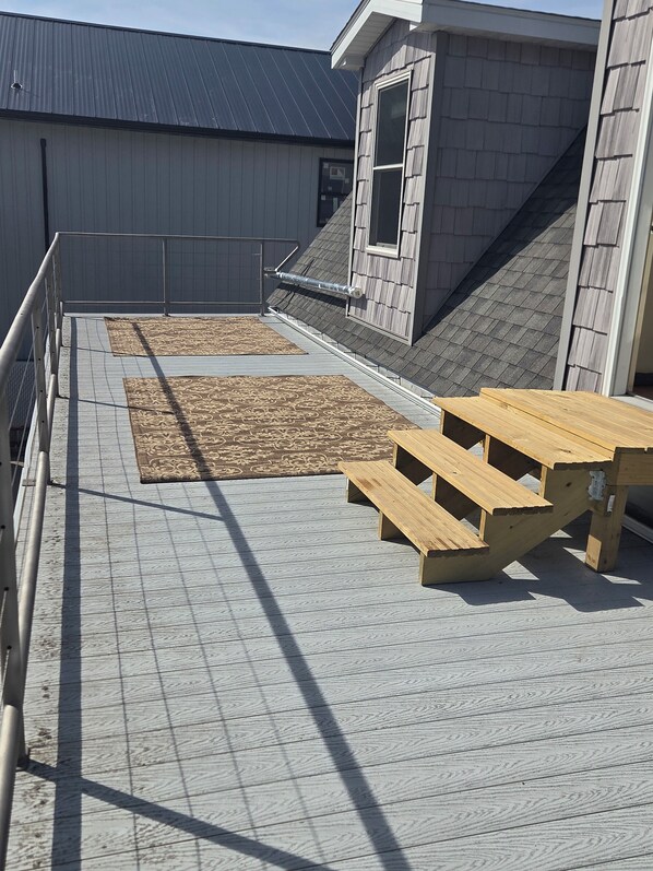 A rooftop terrace with a wooden table and benches, a patterned rug, and a metal railing.