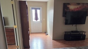 A room with a wooden floor, a door with a curtain, a television mounted on the wall, and a small table with a container. - Cozy 1-bedroom apartment in pleasant Camanche with AC. On the Mississippi River (Camanche)