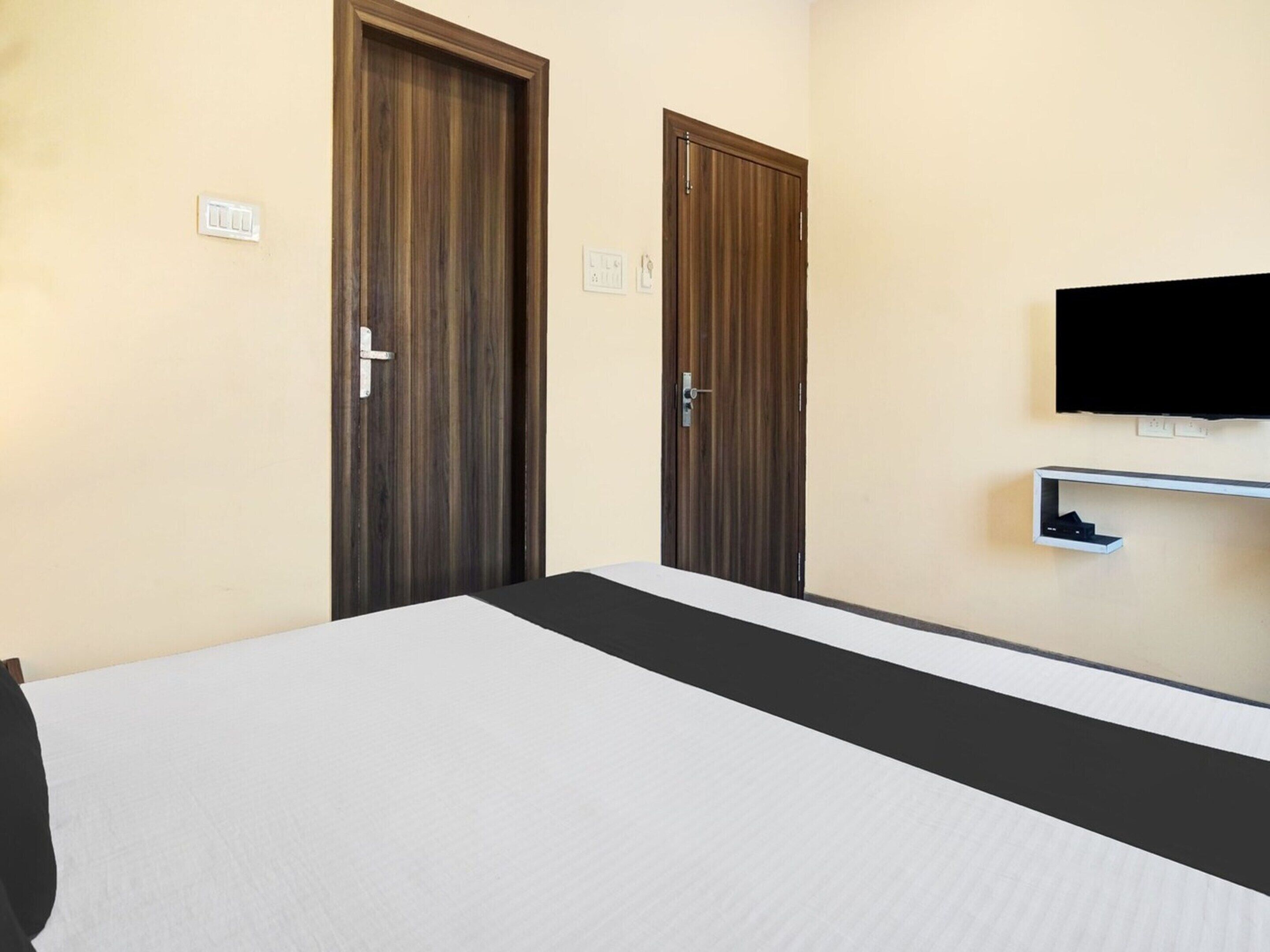 A hotel room with a bed, two wooden doors, a television mounted on the wall, and a small shelf.