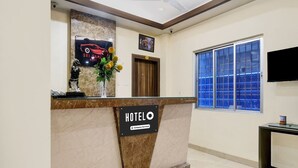 A hotel reception desk with a marble counter, a ceiling fan, a large window with blue-tinted glass, and a television mounted on the wall. - Deluxe Lalganesh Formally Royal Avenue (Guwahati)