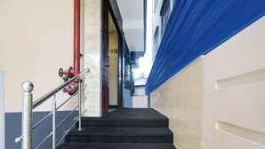 A staircase with a metal handrail, a red fire hose, and an exit sign. - Deluxe Lalganesh Formally Royal Avenue (Guwahati)
