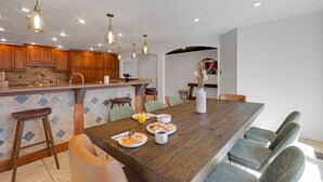 Une cuisine moderne avec des meubles en bois, un grand îlot central, des tabourets de bar et une table à manger avec des chaises.