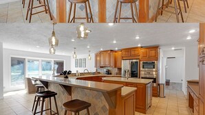 Une cuisine spacieuse avec des meubles en bois, un grand îlot central doté de tabourets et un éclairage suspendu.