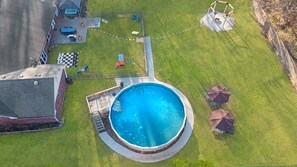 A residential backyard with a swimming pool, a fenced play area, and a patio with outdoor furniture.