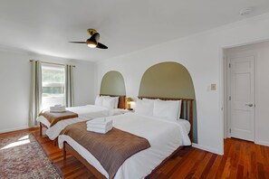A hotel room with two beds, a ceiling fan, a window with curtains, and a door.