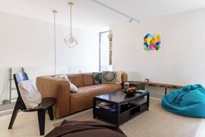 A modern living room with a leather sofa, a black coffee table, a teal bean bag, and a colorful abstract painting on the wall.