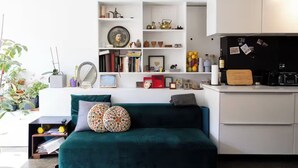 Un espace de vie moderne avec un canapé vert, des étagères blanches et un coin cuisine.