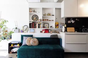 A modern living space with a green sofa, white shelves, and a kitchen area. - Walk to Everything! Bright & Stylish Fully Furnished Stay (Montréal)