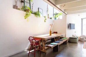 A dining area with a wooden table, benches, and red chairs. There are potted plants on the wall and a television mounted on the wall.