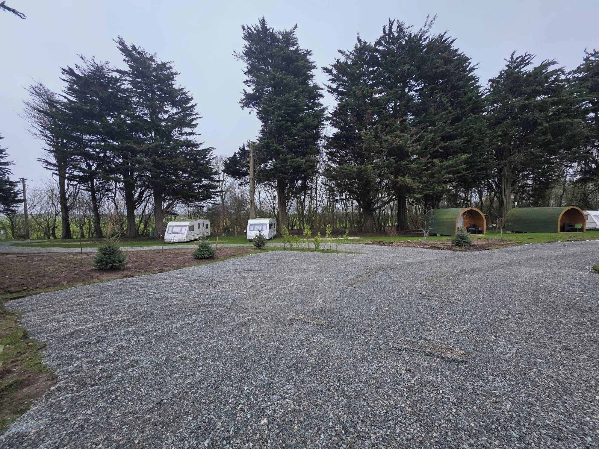 Un’area di parcheggio sterrata con un camper e un edificio a tetto verde, immersa in alberi alti.