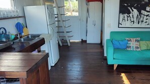 Une cuisine équipée d’un réfrigérateur, d’un évier et d’un comptoir en bois. On y trouve un canapé vert agrémenté de coussins colorés, ainsi qu’un tableau accroché au mur.