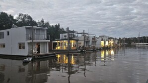 Une propriété située au bord de l’eau, comprenant plusieurs bâtiments, un quai et une étendue d’eau calme dans laquelle se reflètent les constructions.