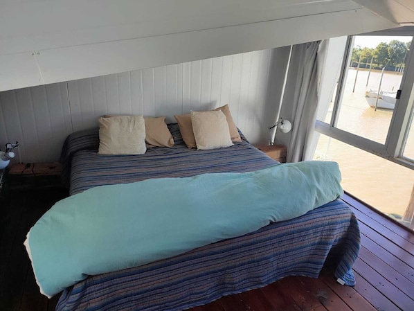 Una cama con ropa de cama a rayas, una lámpara de noche y vistas al exterior.
