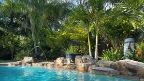 Piscina límpida rodeada por pedras e vegetação tropical.