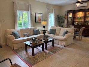 A living room with two sofas, a coffee table, a lamp, a painting, and a cabinet with glassware. - Amazing Private Tropical Pool, Fire Pit, 3 mins to Crystal Beach. (Palm Harbor)