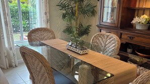 Uma área de refeições com mesa de vidro, cadeiras de vime, uma planta em vaso e um armário de madeira com portas de vidro.