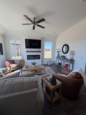 A living room with a ceiling fan, a flat-screen TV, a fireplace, a sofa, a coffee table, and a side table with a pitcher. - Newly Built 3B/2B home in Goose Creek Village 13 mins from UofA Campus (Farmington)
