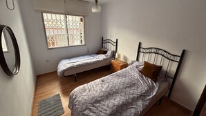 Een slaapkamer met twee eenpersoonsbedden, een nachtkastje met een lamp, een hanglamp, een raam met uitzicht en een spiegel aan de muur.