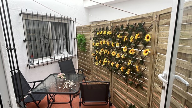 Een glazen tafel met stoelen, een houten hek met zonnebloemen en een raam met tralies.