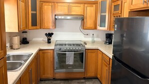Une cuisine avec des meubles de rangement en bois, une cuisinière en acier inoxydable, un réfrigérateur et une machine à café.
