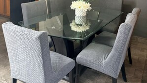 Un espace de salle à manger moderne avec une table en verre, des chaises à revêtement gris et un luminaire suspendu.