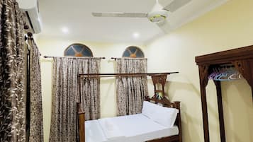 A bedroom with a bed, ceiling fan, air conditioning unit, curtains, and a wooden wardrobe.