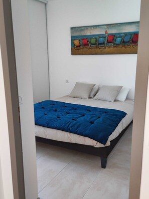 Ein Schlafzimmer mit einem Bett, einem Bild von Strandstühlen und einem gefliesten Boden.