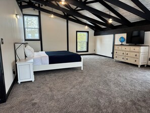 Une chambre à coucher comprenant un lit, une table de chevet, une commode, un téléviseur et de grandes fenêtres.