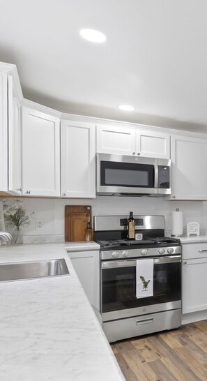 Une cuisine moderne avec des meubles blancs, un four en acier inoxydable, un micro-ondes et une planche à découper en bois.