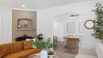 A living room with a sofa, a coffee table with books, a fireplace, and a dining area with a table and chairs.