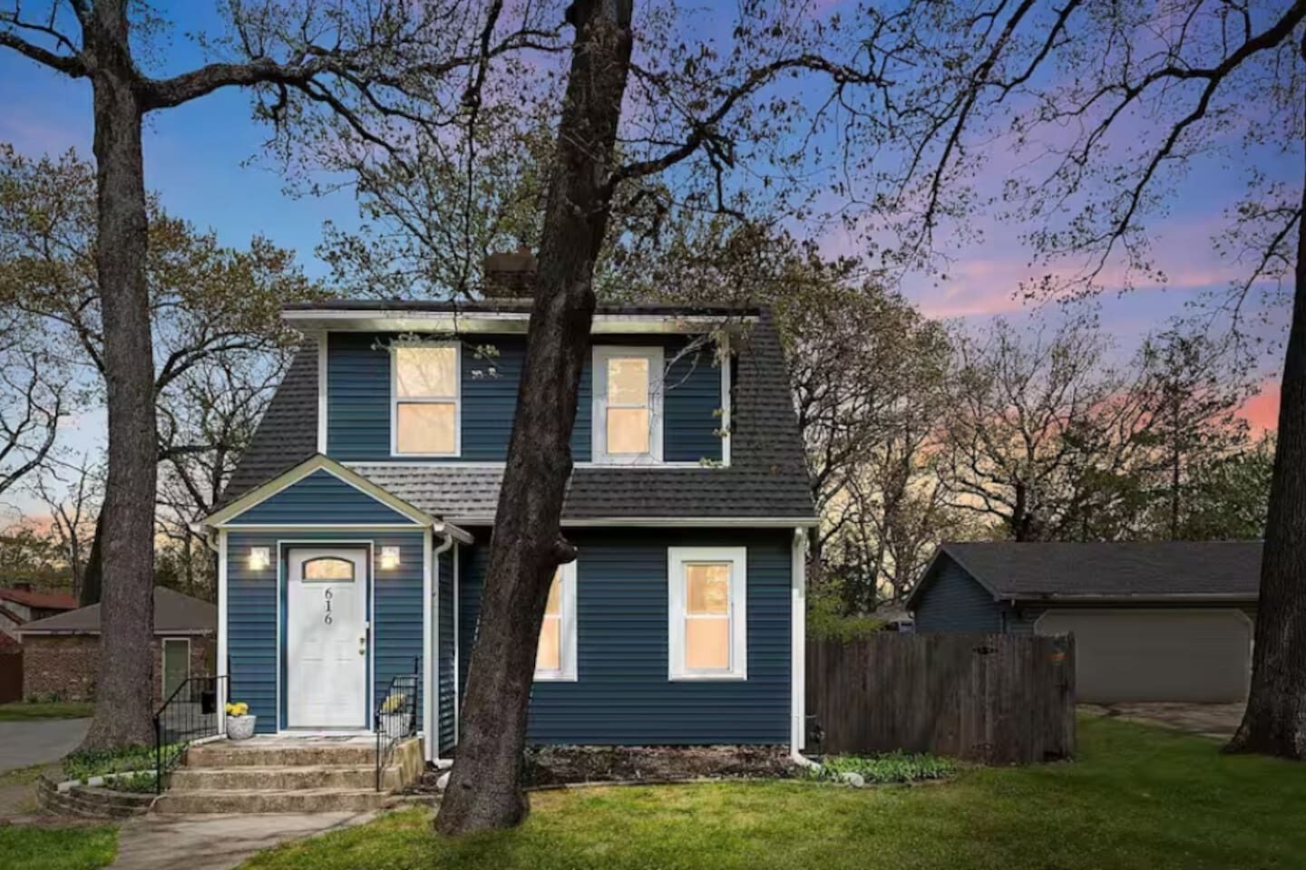 Une maison à deux étages avec un porche à l’avant et un petit jardin devant.