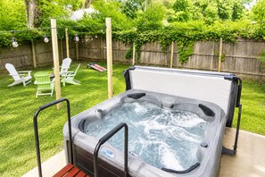 Un bain à remous doté d’une terrasse en bois, entouré d’une clôture en bois et de verdure.