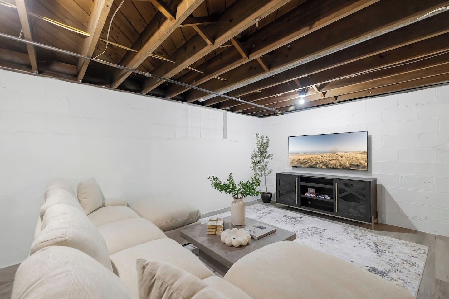 A modern living room with a sectional sofa, a flat-screen TV mounted on a white brick wall, and a minimalist entertainment unit.