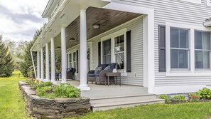 Ein Haus mit überdachter Veranda, Steinpflanzgefäß und Gartenmöbeln.