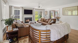 Ein Wohnzimmer mit Kamin, Ledersofa, Holzstuhl und einem großen Fenster.
