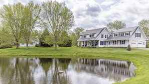 A large, two-story house with a covered porch and a pond in front. - Country House with Pond, Mountain Views, Mins to Stowe Center (Morristown)