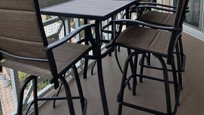 Varanda com mesa e cadeiras, vista para uma praia e um edifício.