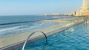 Una piscina sul tetto con barriera in vetro, con vista sulla spiaggia e sullo skyline cittadino.