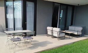 A modern outdoor patio with a table and chairs, a sofa, and a large sliding glass door. - Ellipse Waterfall ~ Power & Water Backup, Free WiFi, next to Mall of Africa (Midrand)