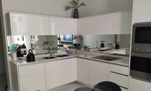 A modern kitchen with white cabinetry, a central island with a sink, and a built-in oven. - Ellipse Waterfall ~ Power & Water Backup, Free WiFi, next to Mall of Africa (Midrand)