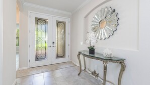 Un corridoio con una porta in vetro, uno specchio decorativo e un tavolo consolle con una pianta in vaso.