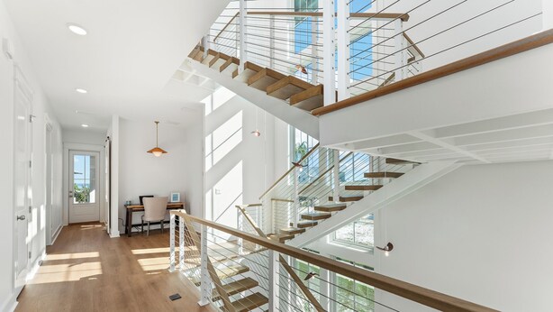 Ein modernes Interieur mit Treppe, Holzboden und großen Fenstern, die viel Tageslicht hereinlassen.