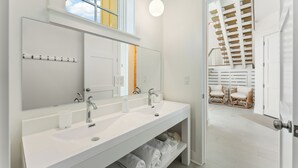 Ein modernes Badezimmer mit zwei Waschbecken, einem großen Spiegel und Blick auf eine Holztreppe, die zu einem Balkon führt.
