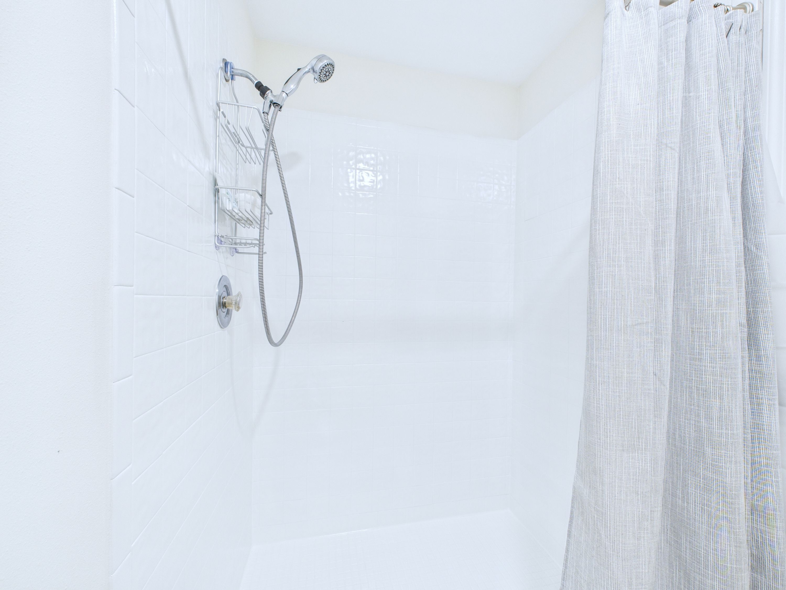 A shower with a handheld showerhead and a wall-mounted faucet, a towel rack, and a shower curtain.