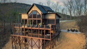 A multi-story wooden cabin with a balcony, large windows, and a view of the surrounding landscape. - Luxury Smoky Mountain Cabin w/ Sauna (Sevierville)