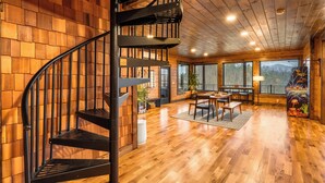 A wooden interior with a spiral staircase, a dining area, and large windows. - Luxury Smoky Mountain Cabin w/ Sauna (Sevierville)