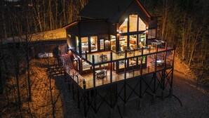 A two-story cabin with a balcony, large windows, and a deck area. - Luxury Smoky Mountain Cabin w/ Sauna (Sevierville)